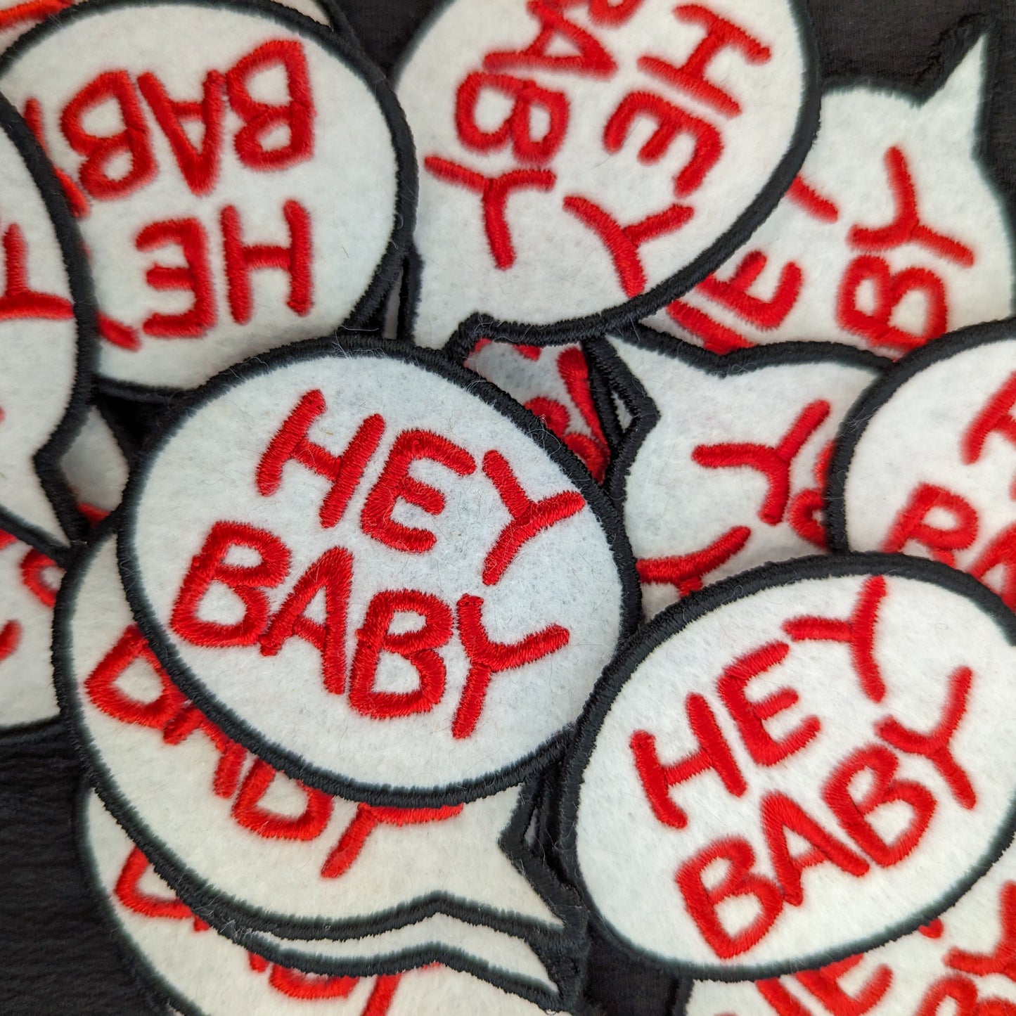 White felt "HEY BABY" speech bubble patches with red embroidery and black borders.