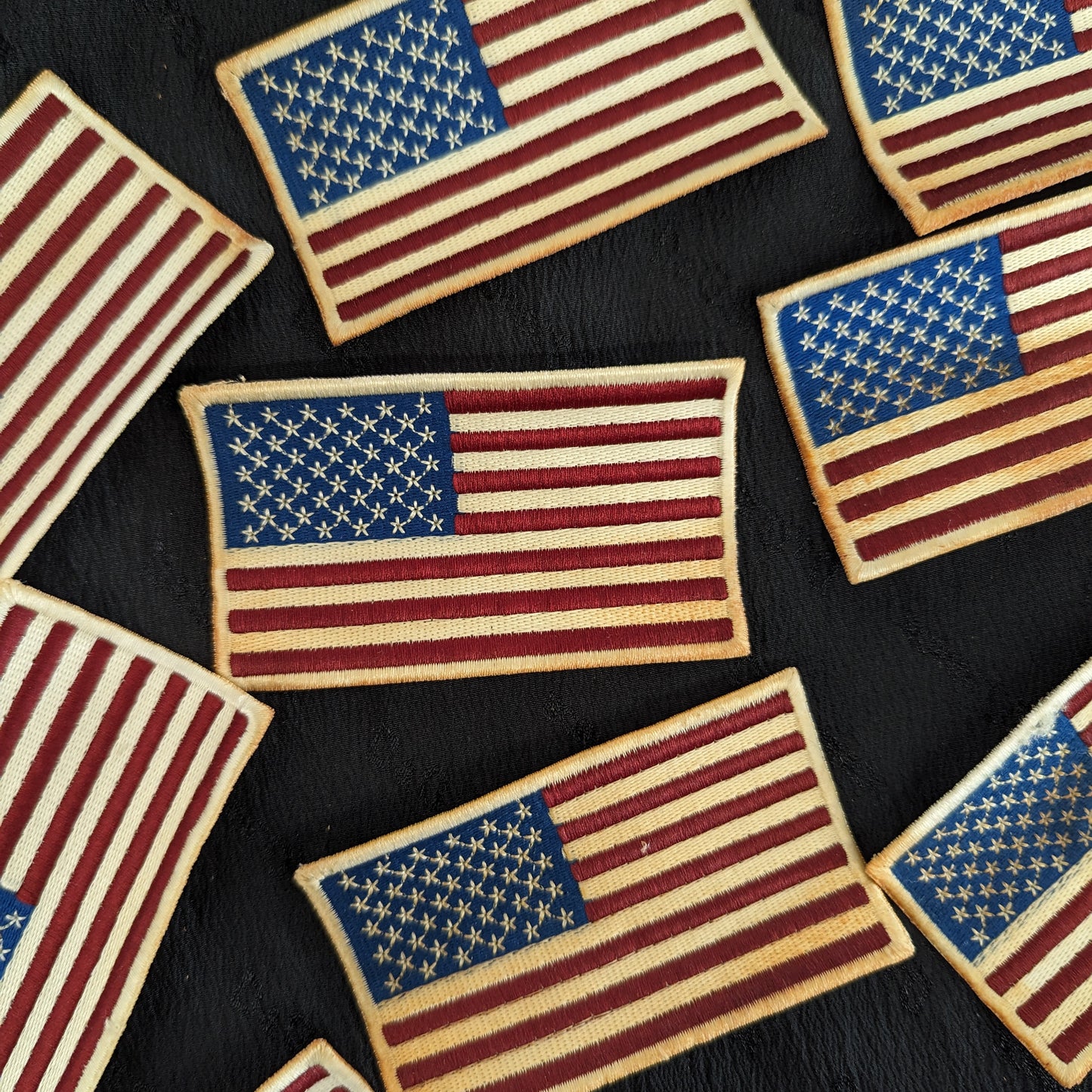 Embroidered USA flag patches, red, white, and blue, with distressed edges on a dark background.