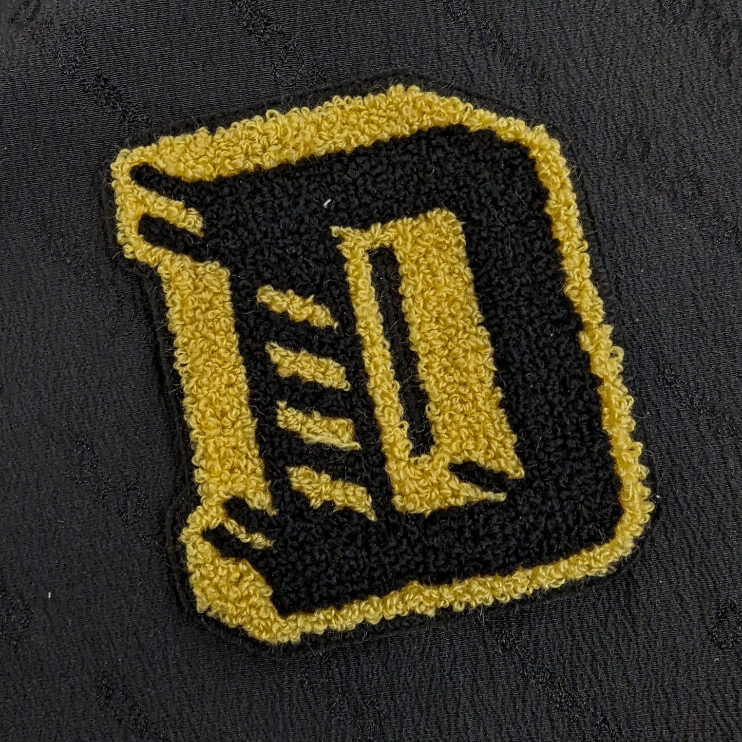 Black and gold chenille letter D patch, 8x8cm, on a dark fabric background.