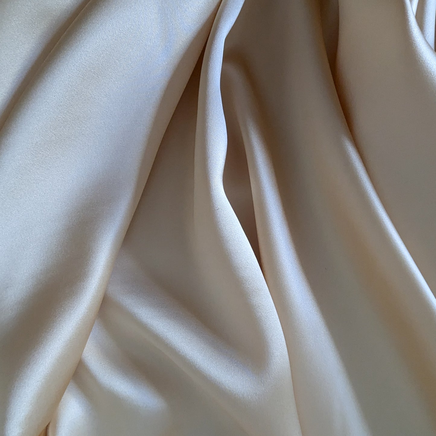 Draped heavy satin silk fabric in a light beige or champagne color, showing its smooth, lustrous texture.