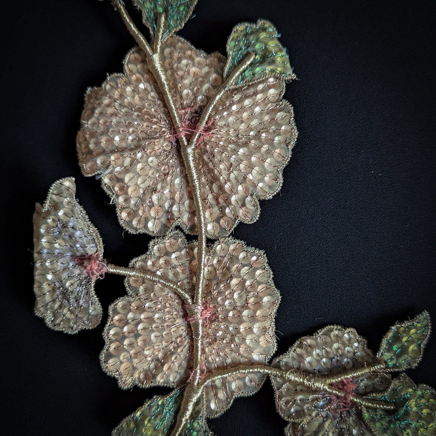 D&G 15x19cm sequin flower appliqué with gold wire stem and green leaves on black fabric.