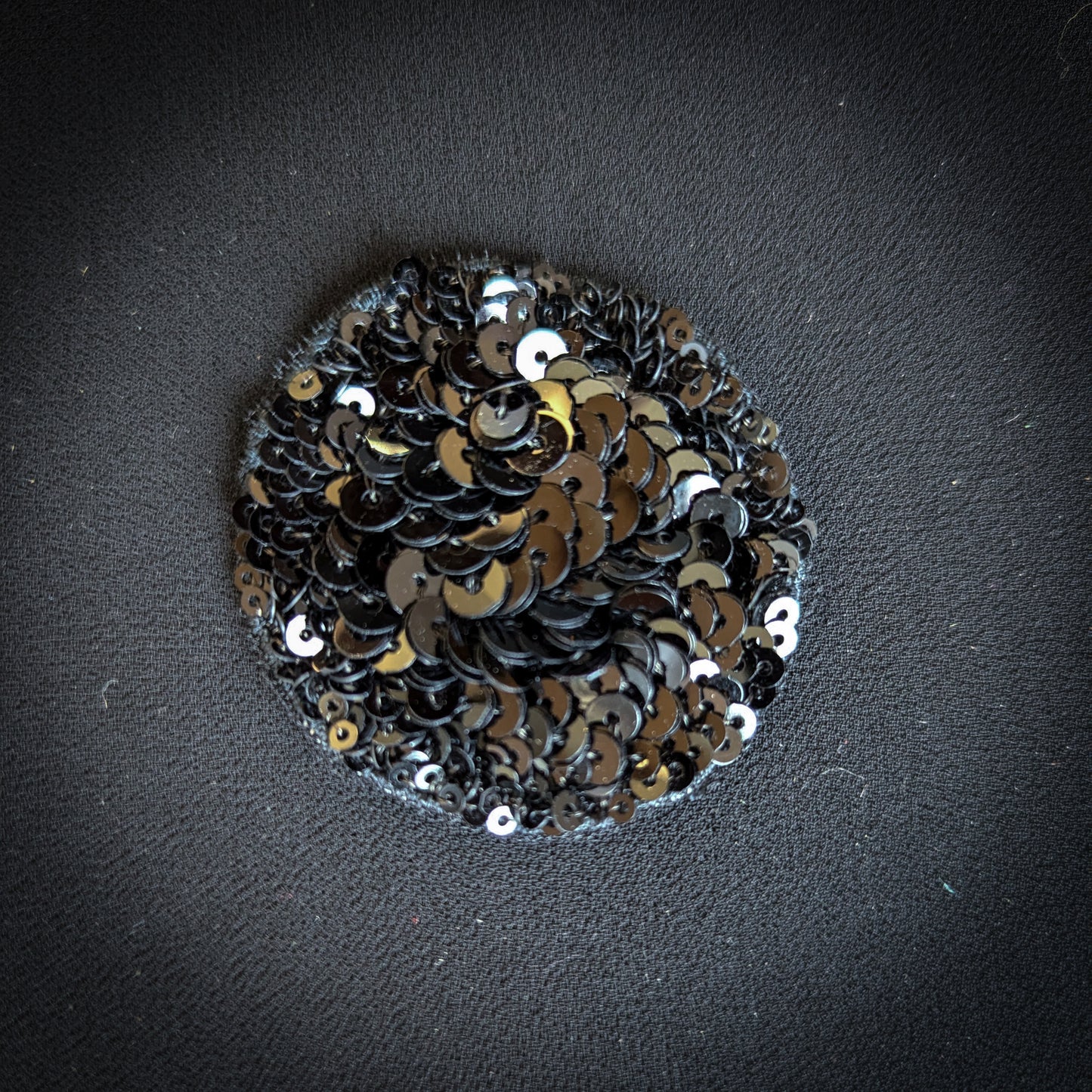 Round D&G black sequin patch, 5x5 cm, on dark fabric.
