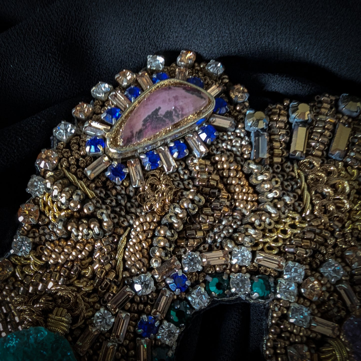Heavy patch with pink, blue, and clear gemstones, gold beads, and intricate embroidery on black fabric.