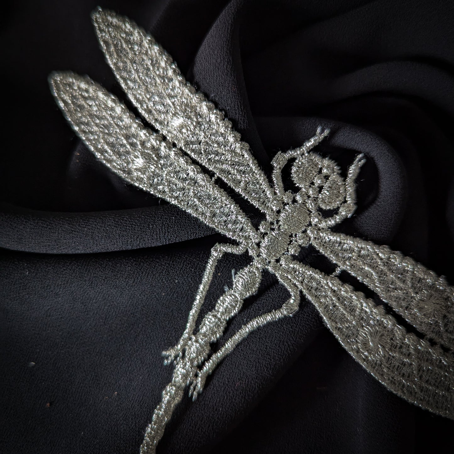 Silver embroidered dragonfly patch, 9x15cm, on a black fabric background.