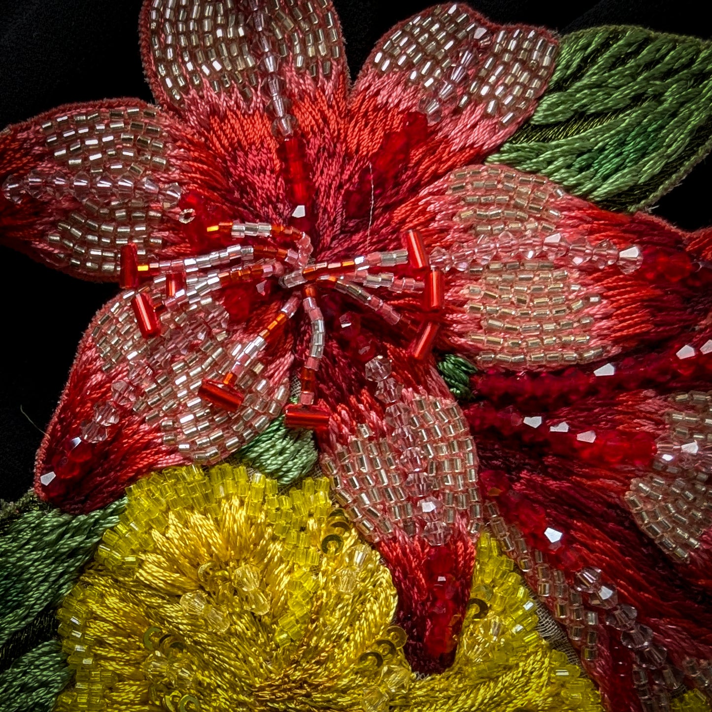 Embroidered floral patch with red petals, clear beads, yellow center, and green leaves.