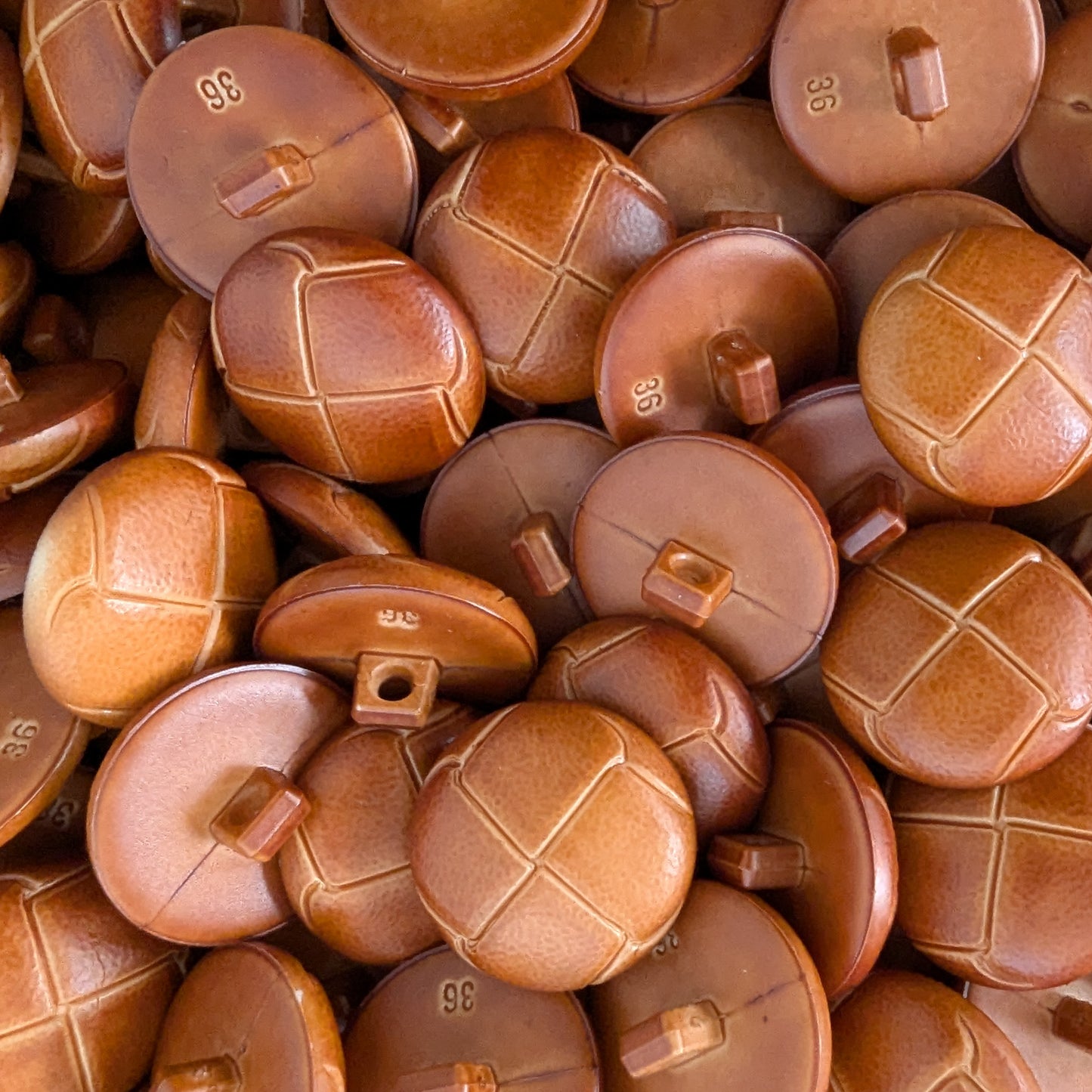 Pile of round brown plastic buttons with a leather-look finish, some with cross-stitch texture, some smooth.