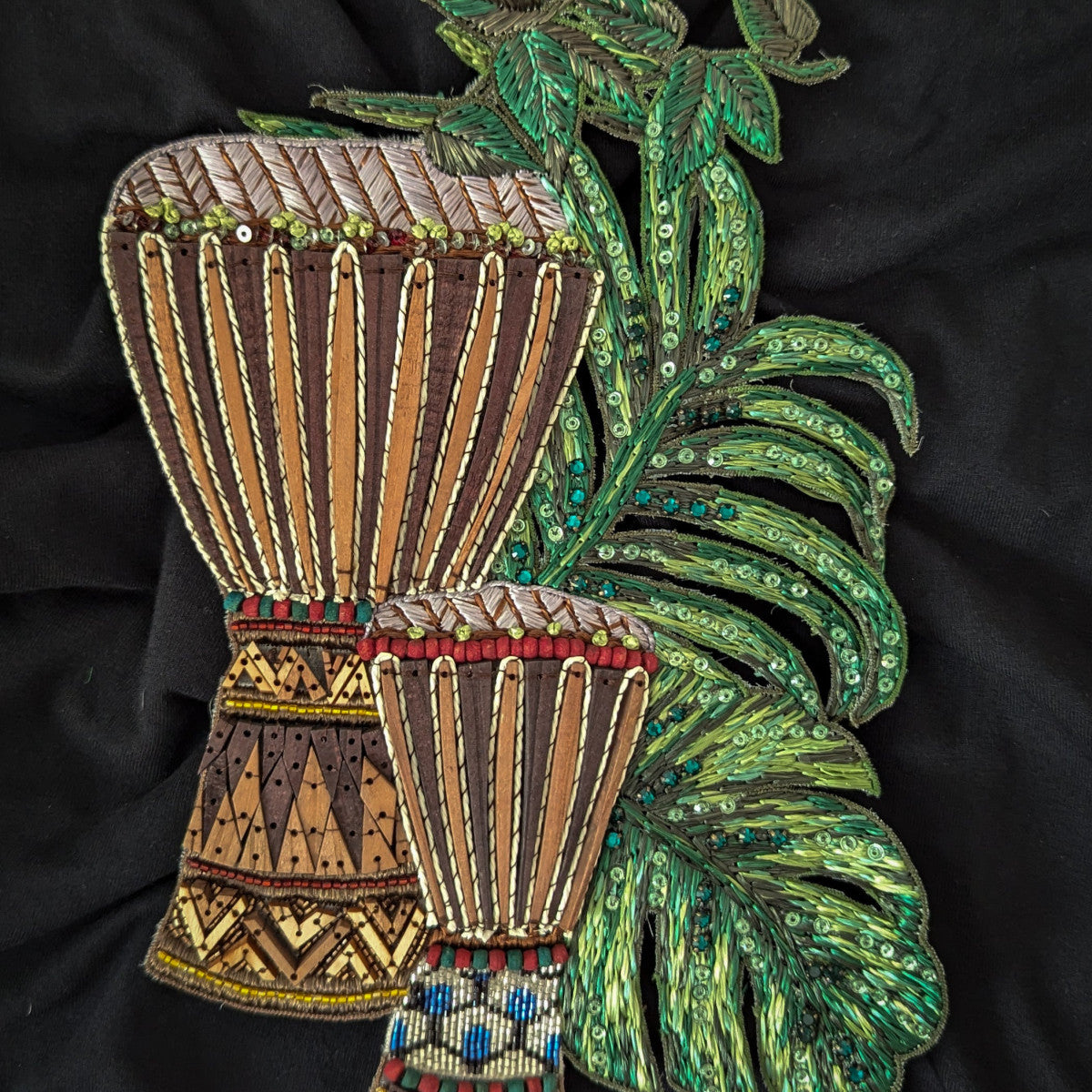 Embroidered D&G patch with two brown drums, wood, beads, and green sequined leaves on black fabric.