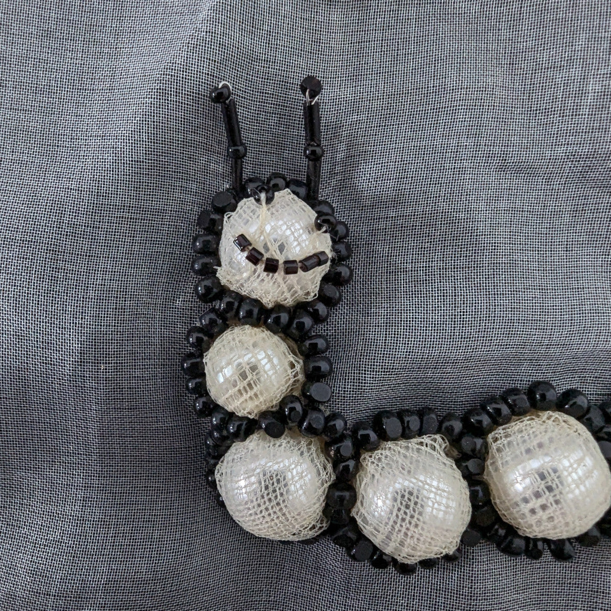 Black and white beaded caterpillar patch with pearl-like segments and antennae, 10 cm.
