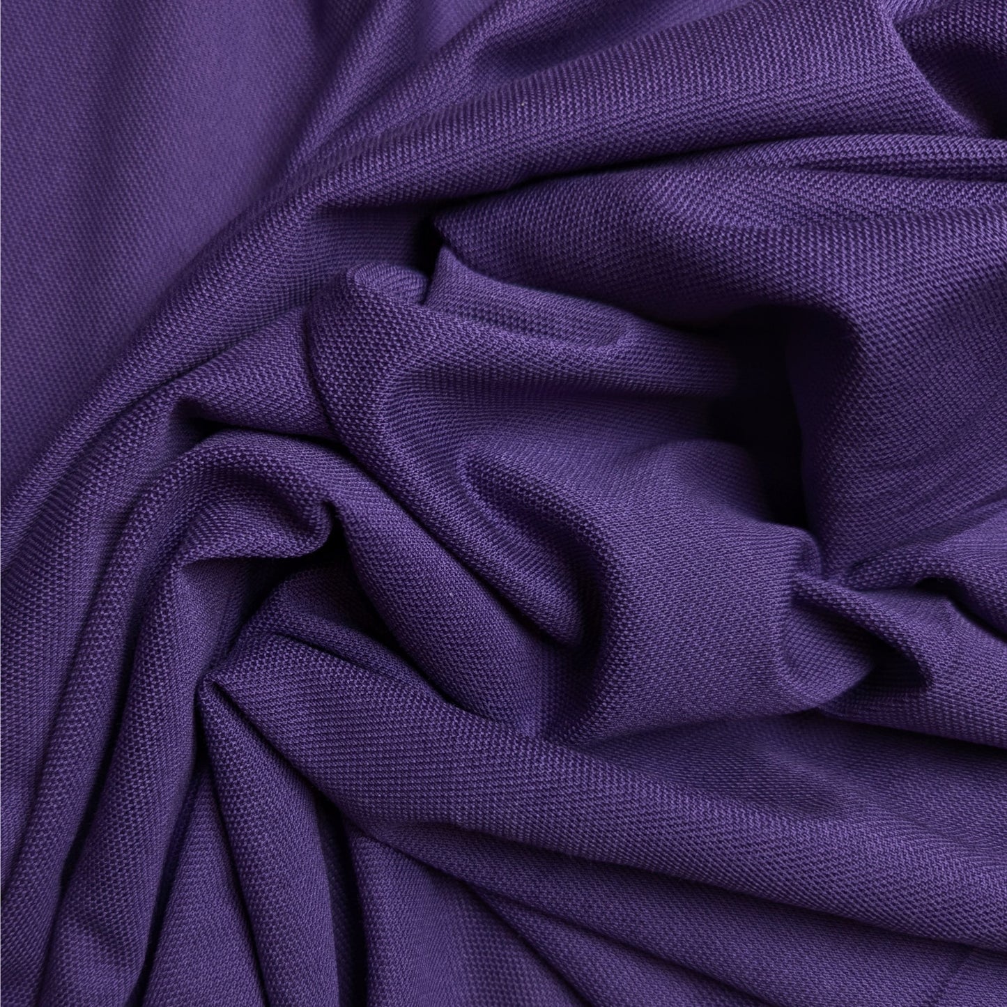 Textured purple cotton piqué fabric, draped and folded, showing its distinct weave.