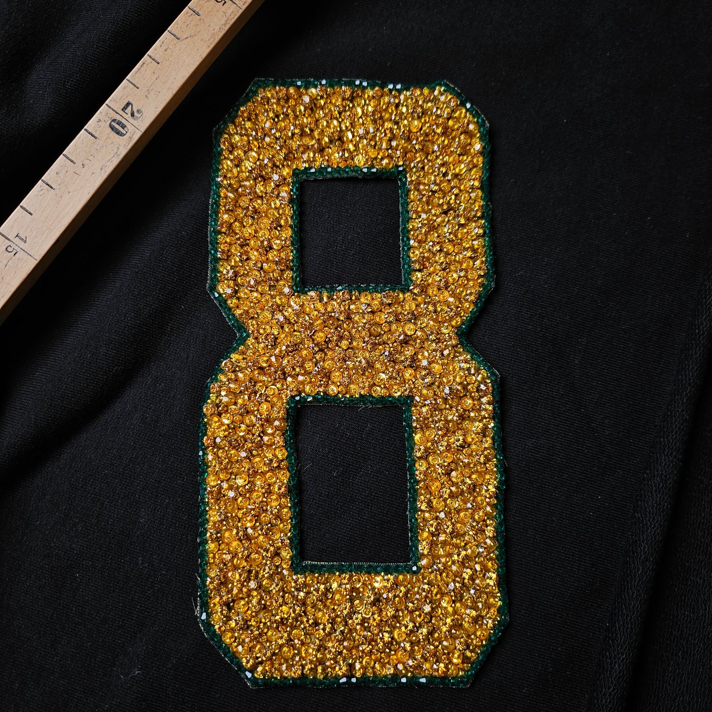 Gold sequin and stone "8" patch with green border, 10x19cm, on black fabric.