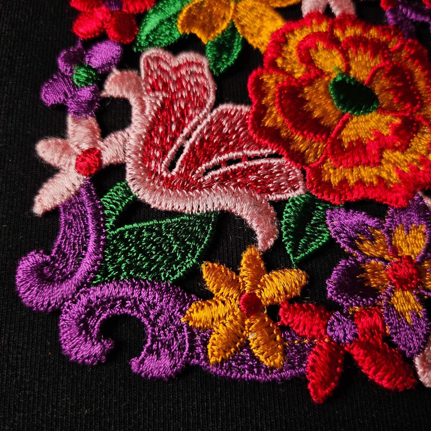 Colorful embroidered floral patch with red, yellow, pink, purple, and green flowers and leaves.
