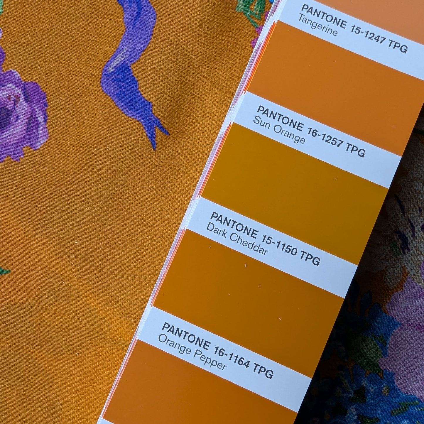 Dark cheddar silk crepe de chine fabric with purple floral print, next to a Pantone color swatch.