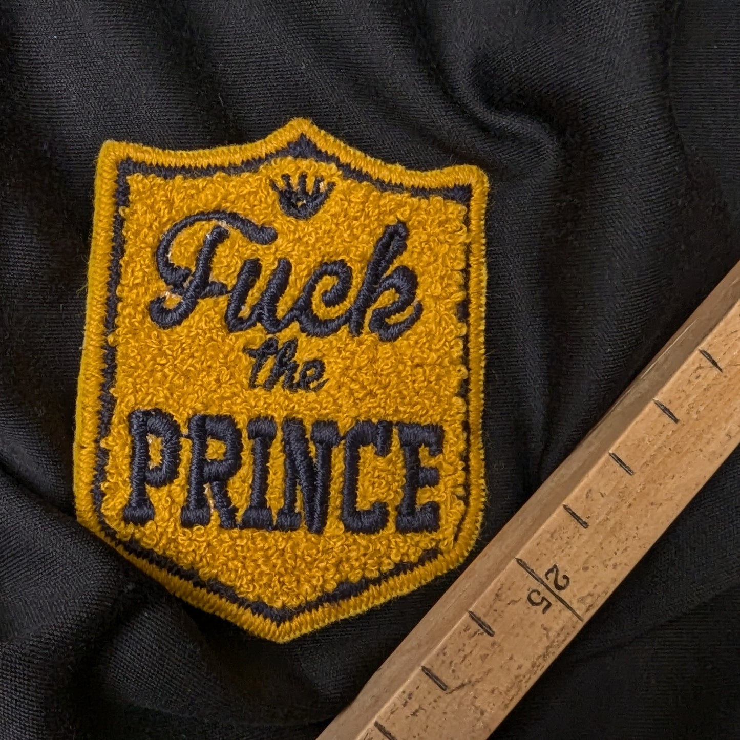 Mustard yellow D&G "Fuck the Prince" patch with 3D terrycloth texture and dark blue embroidery.