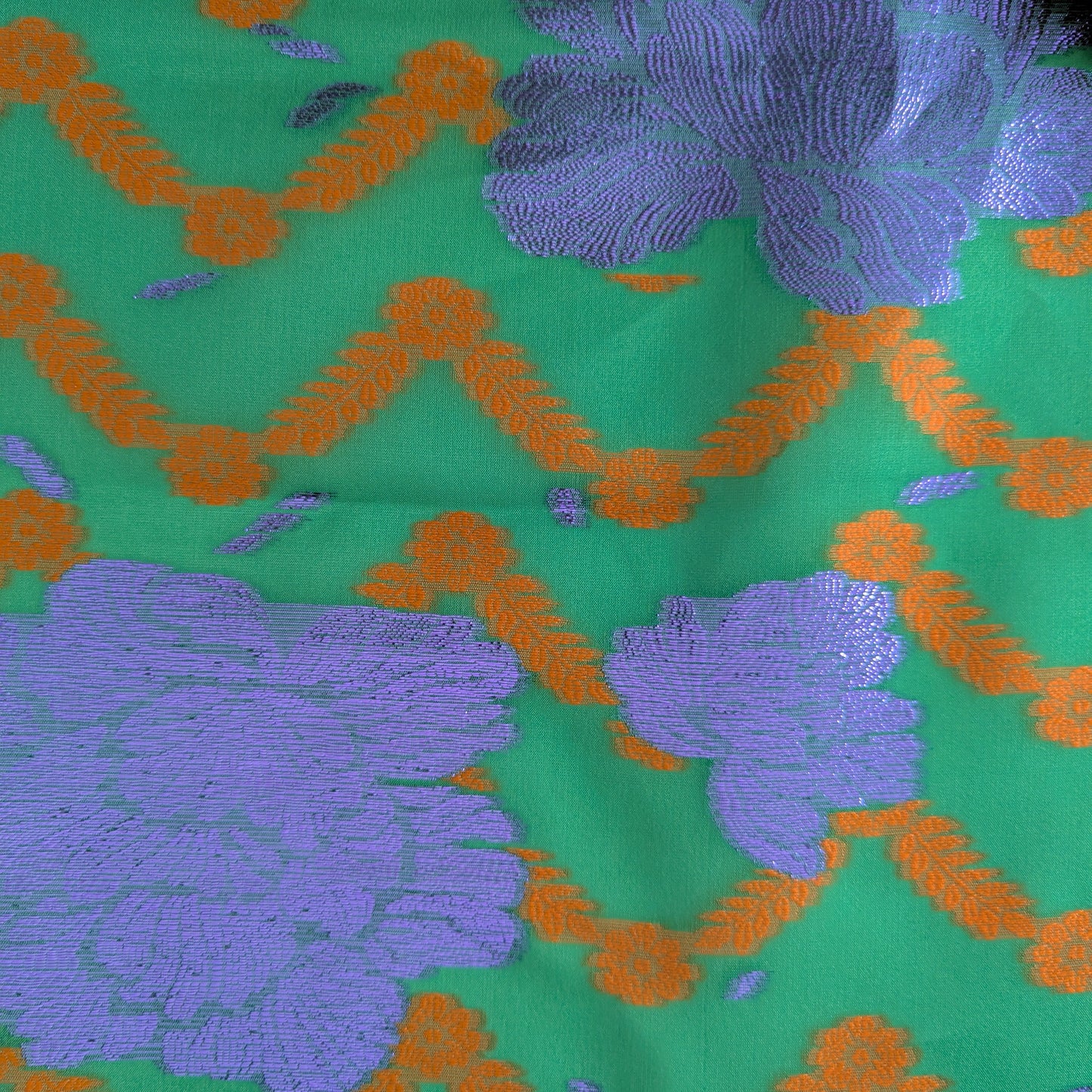 Green jacquard silk fabric with shimmering purple floral and orange geometric Lurex patterns.