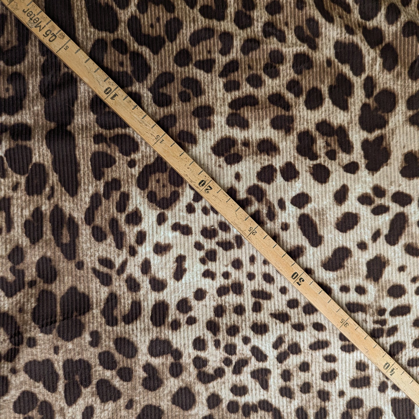 D&G deadstock corduroy fabric with a brown leopard print and a wooden measuring tape.