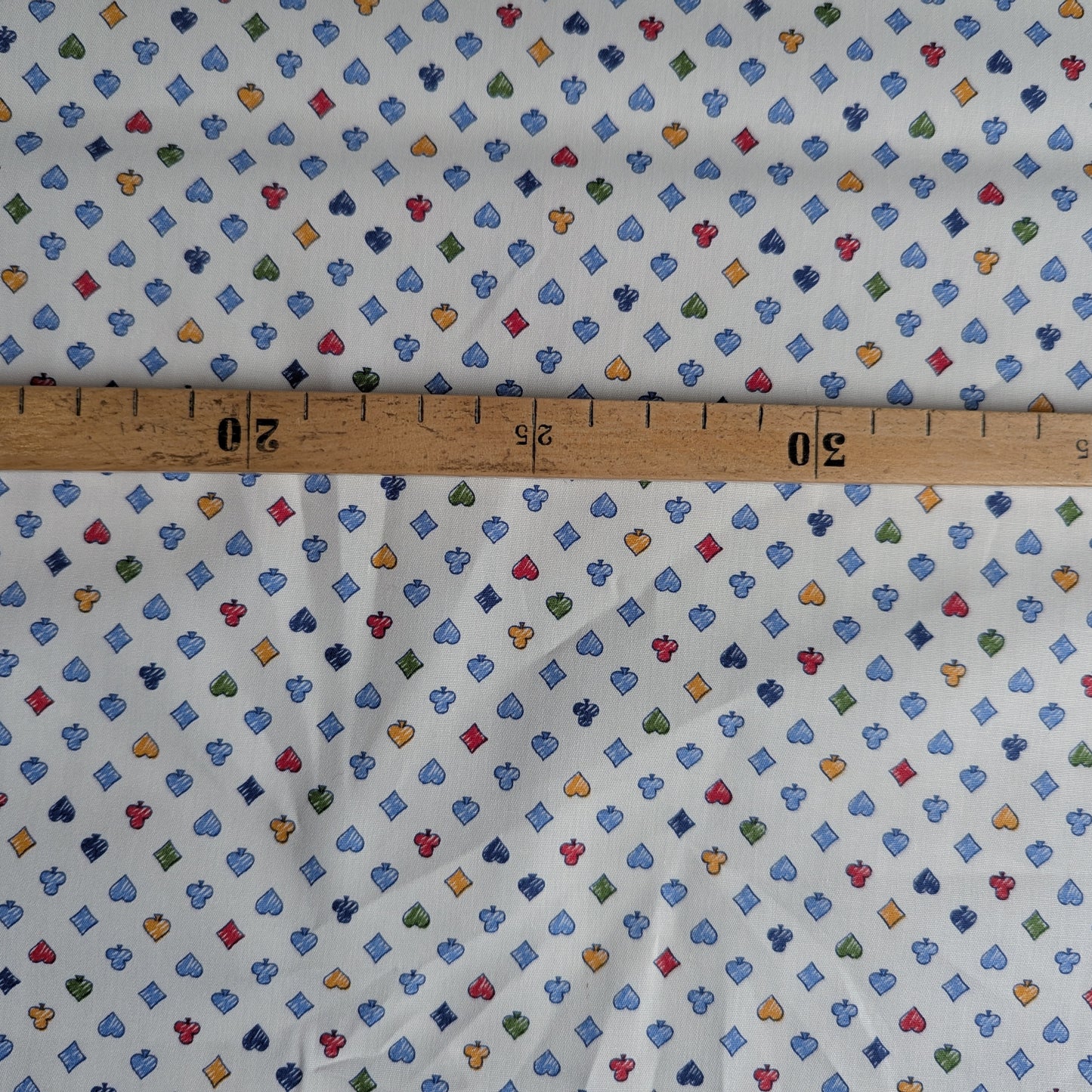 White cotton poplin fabric with colorful playing card suit motifs, measured by a wooden ruler.