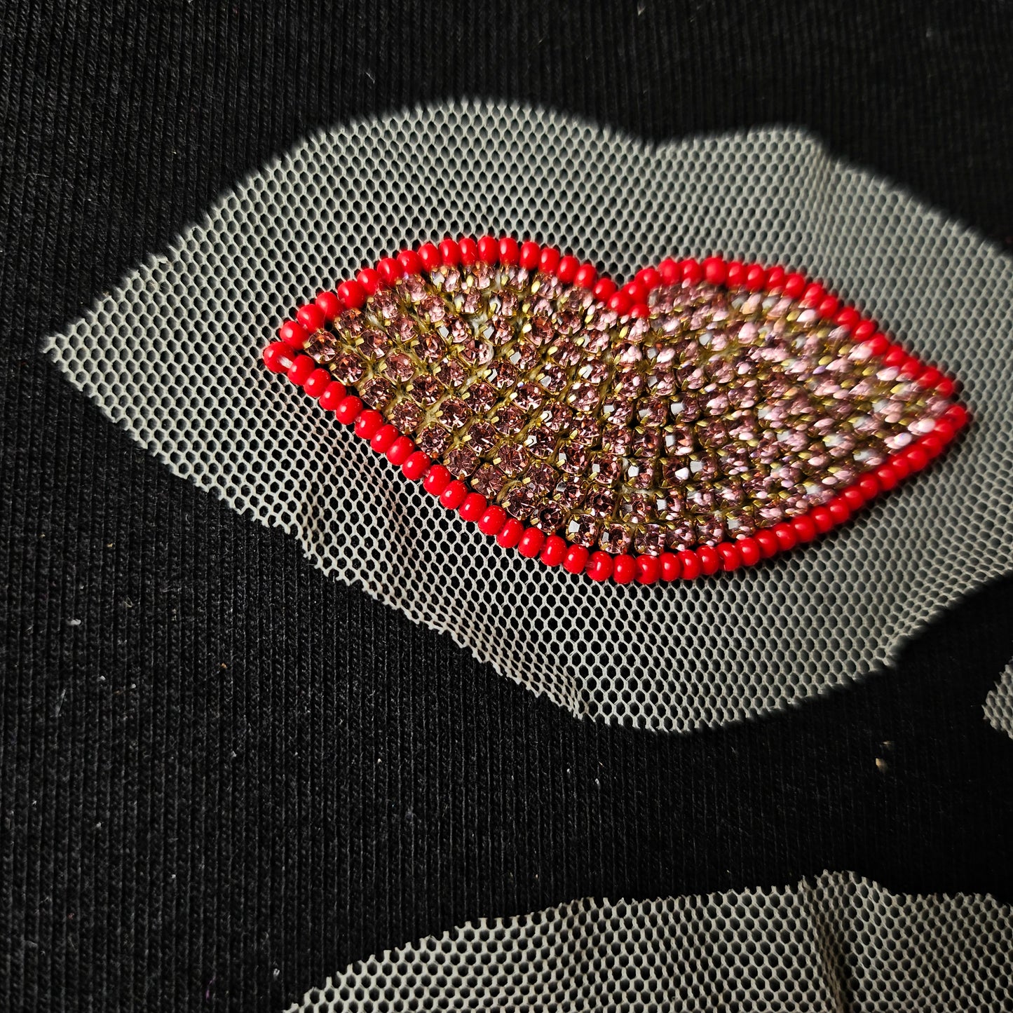 Sparkling pink crystal lip patch with red beaded outline on sheer white mesh, on black fabric.