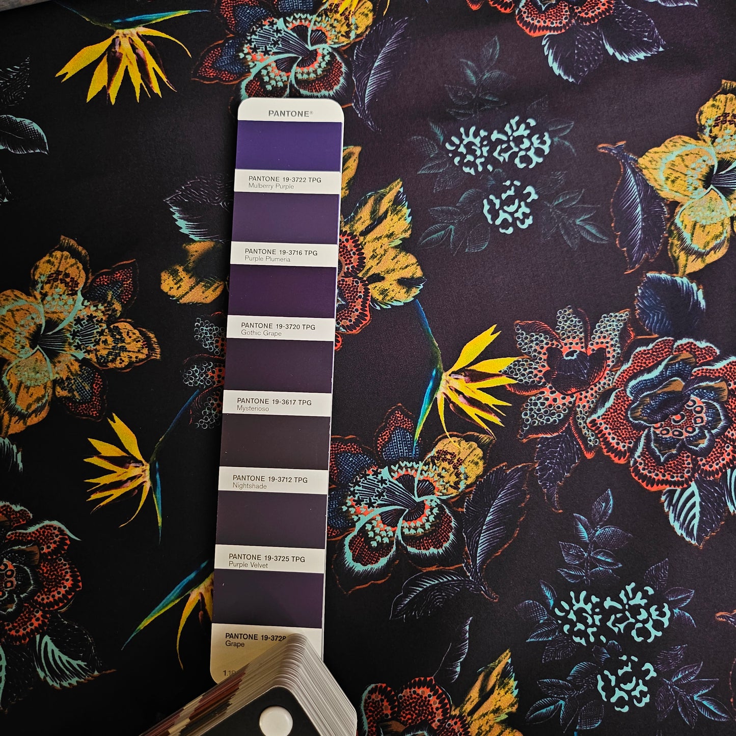 Dark purple parachute silk fabric with vibrant yellow, orange, and blue floral patterns, next to a Pantone color swatch.