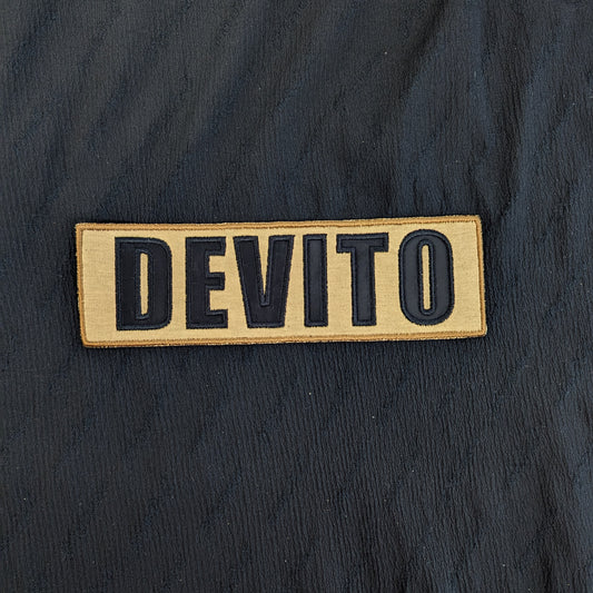 Embroidered "DEVITO" patch, 17x5.5cm, with black letters on a tan mixed fabric background.