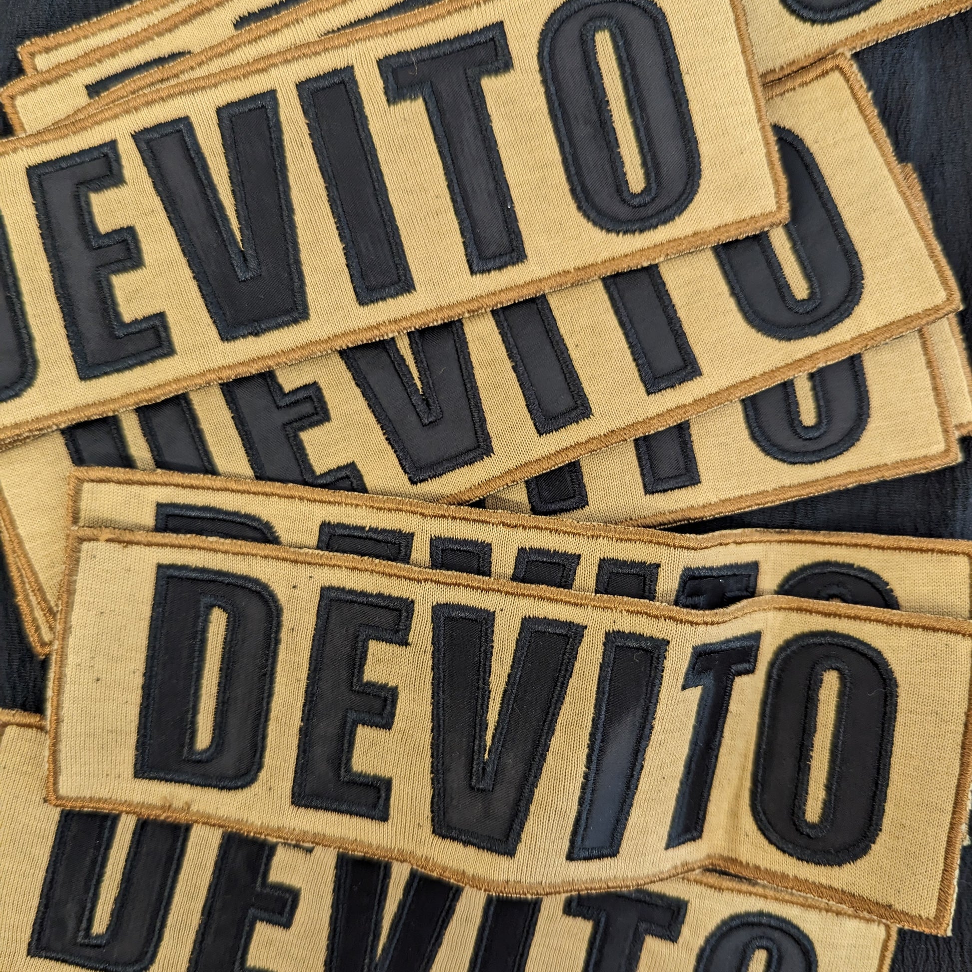 Embroidered "DEVITO" patch, 17x5.5cm, with black letters on a tan fabric background.