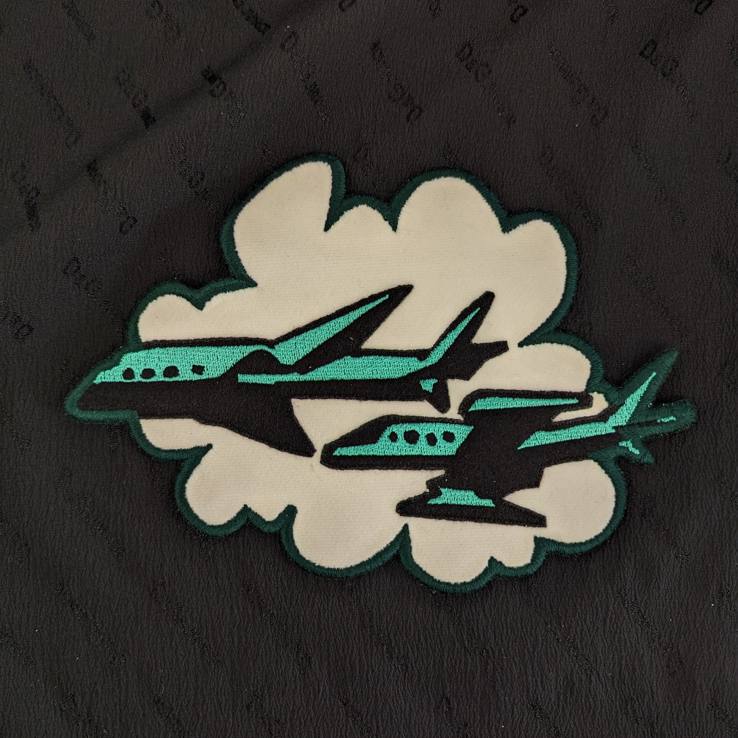 Designer deadstock patch: black and teal planes flying through a white cloud, 20x14cm.