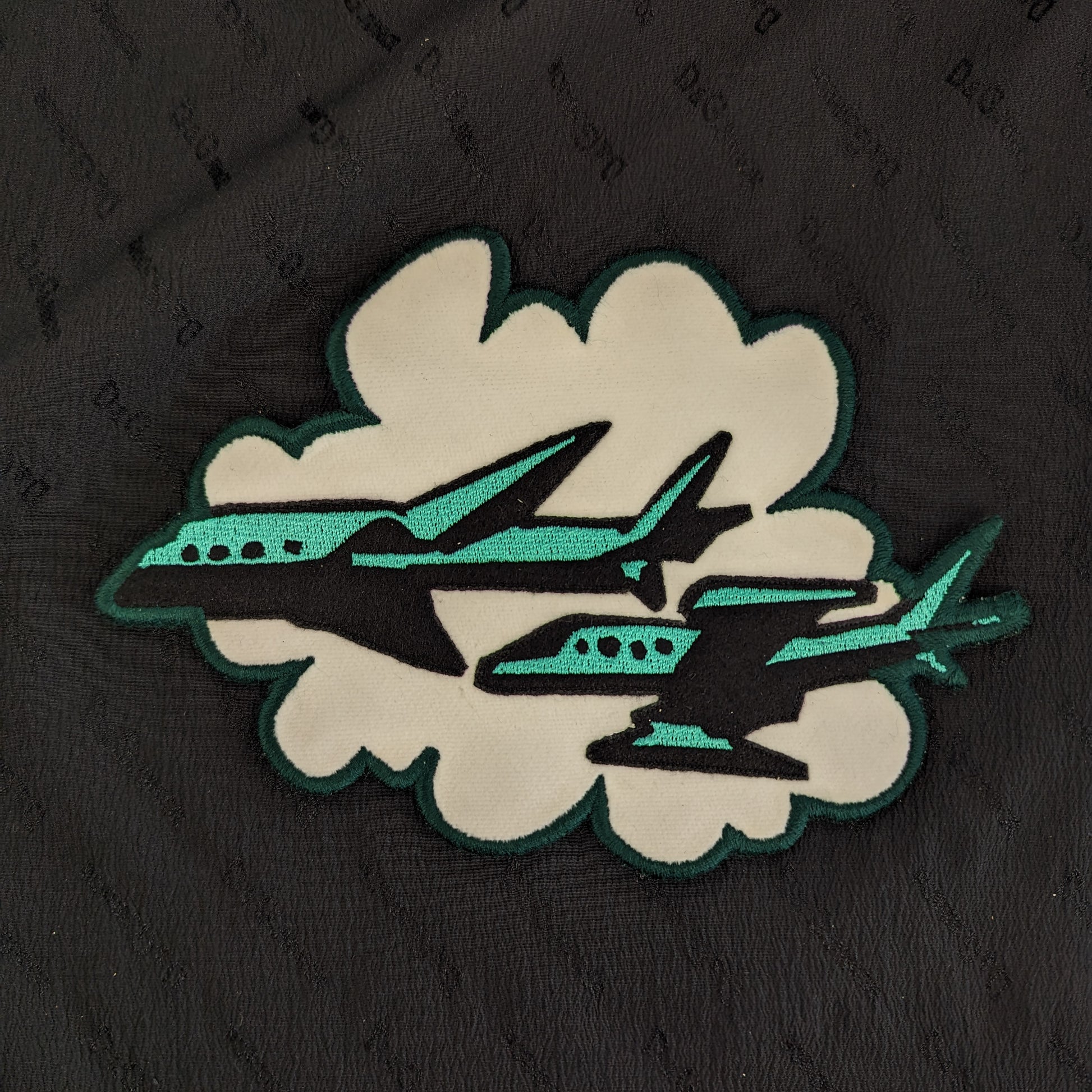 Designer deadstock patch: black and teal planes flying through a white cloud, 20x14cm.