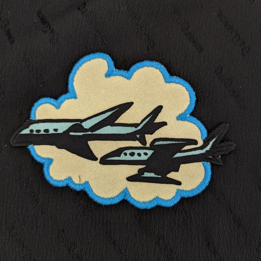 Black, tan, and blue DG Flugzeuge patch with two airplanes on a cloud, 13x9cm.