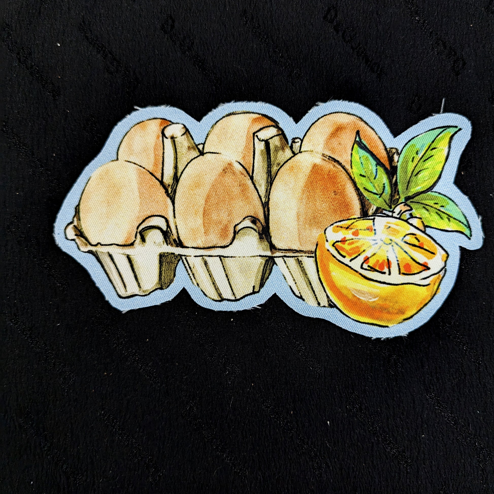 D&G egg carton patch with six brown eggs and a sliced orange with green leaves, 15x8cm.