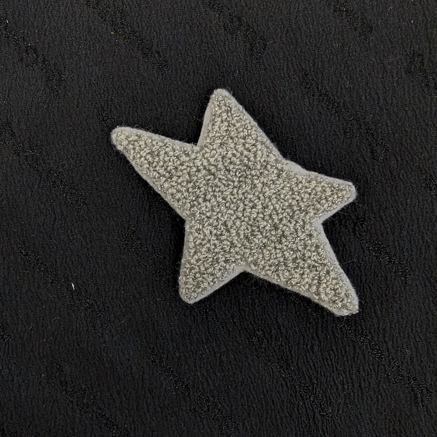 Silver textured star patch, 8x8 cm, on a black fabric background.