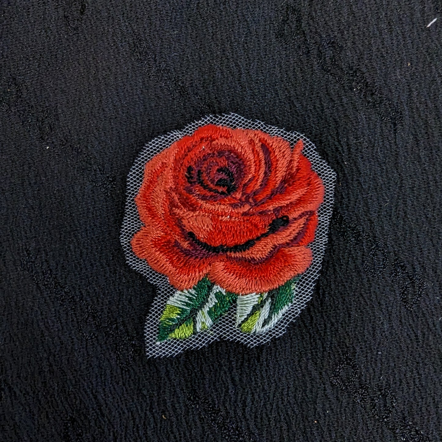 Red embroidered rose patch with green leaves, 4x4 cm, on a black textured background.
