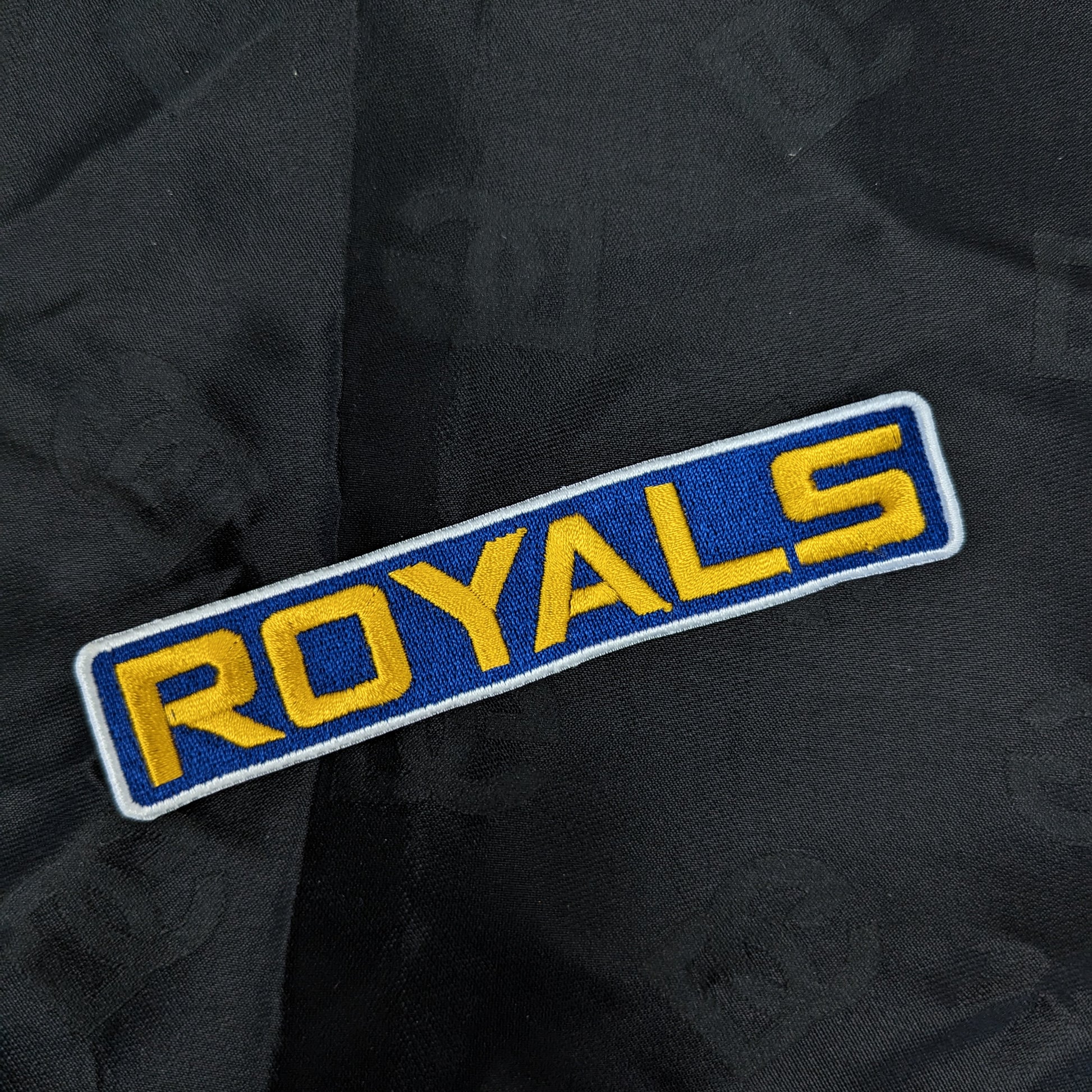 Blue and yellow "ROYALS" embroidered patch, 12x2cm, on black fabric.