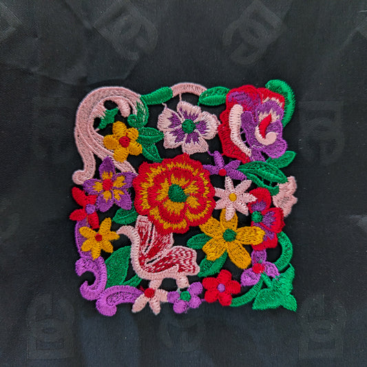 Colorful embroidered floral patch with a bird design, about 12 cm square, on a black background.