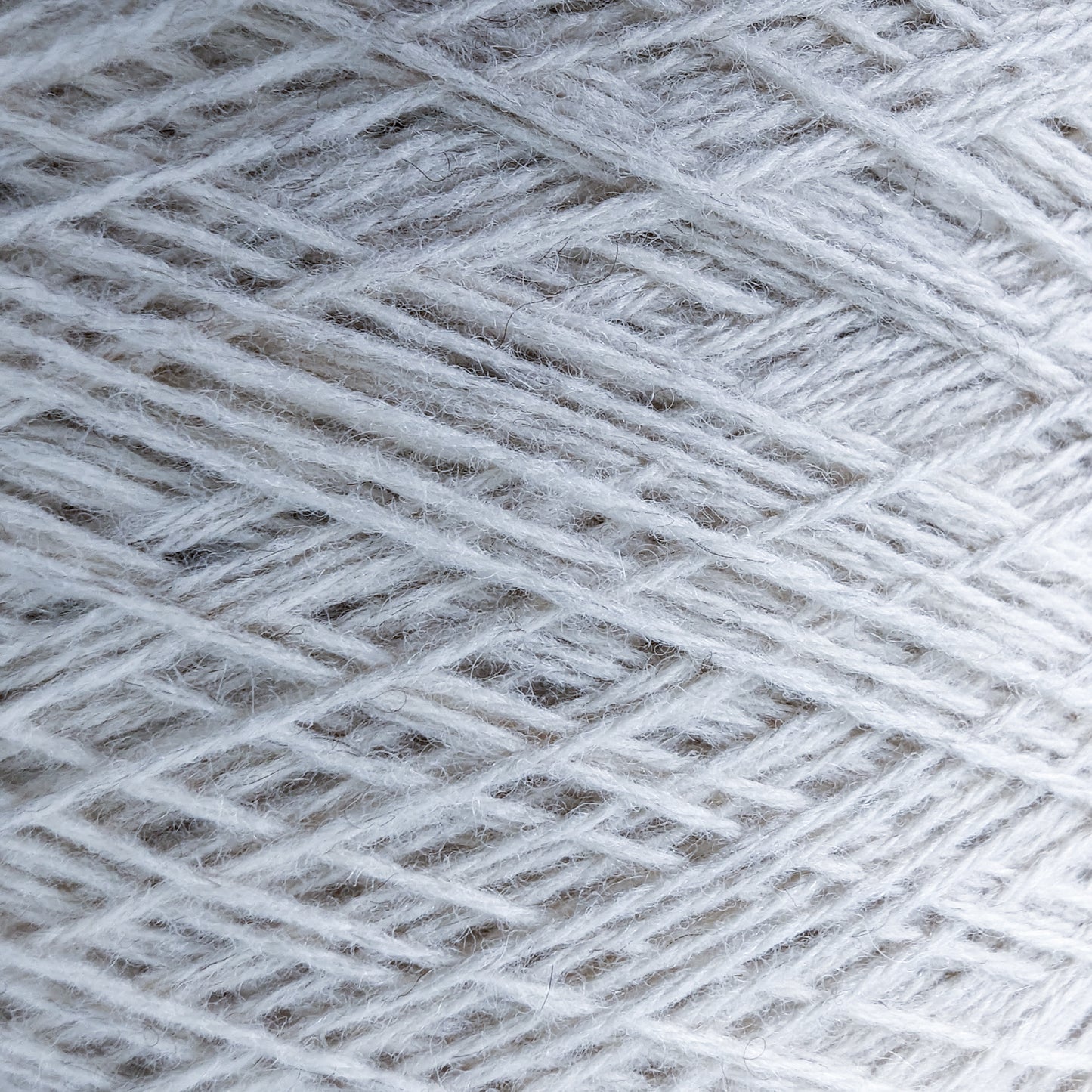 Close-up of natural white 50% yak, 50% merino yarn on a cone, showing its soft texture.