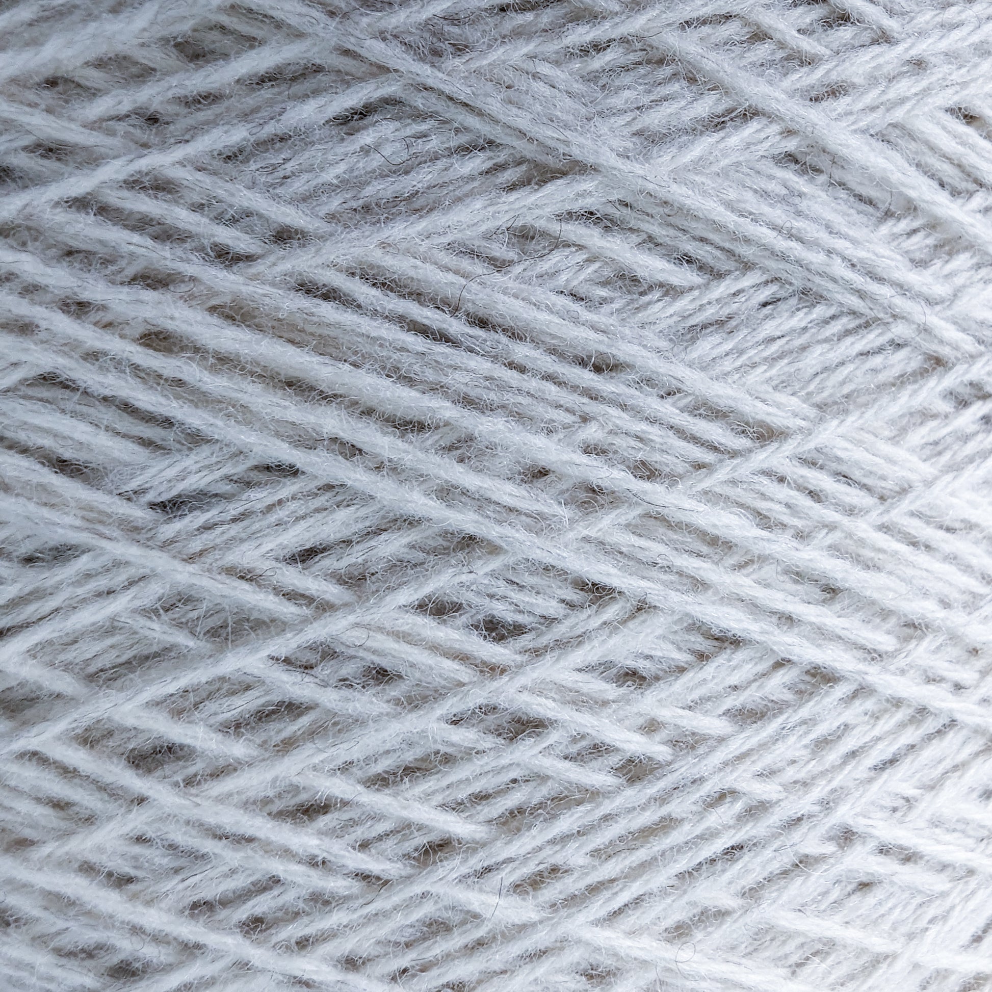 Close-up of natural white 50% yak, 50% merino yarn on a cone, showing its soft texture.
