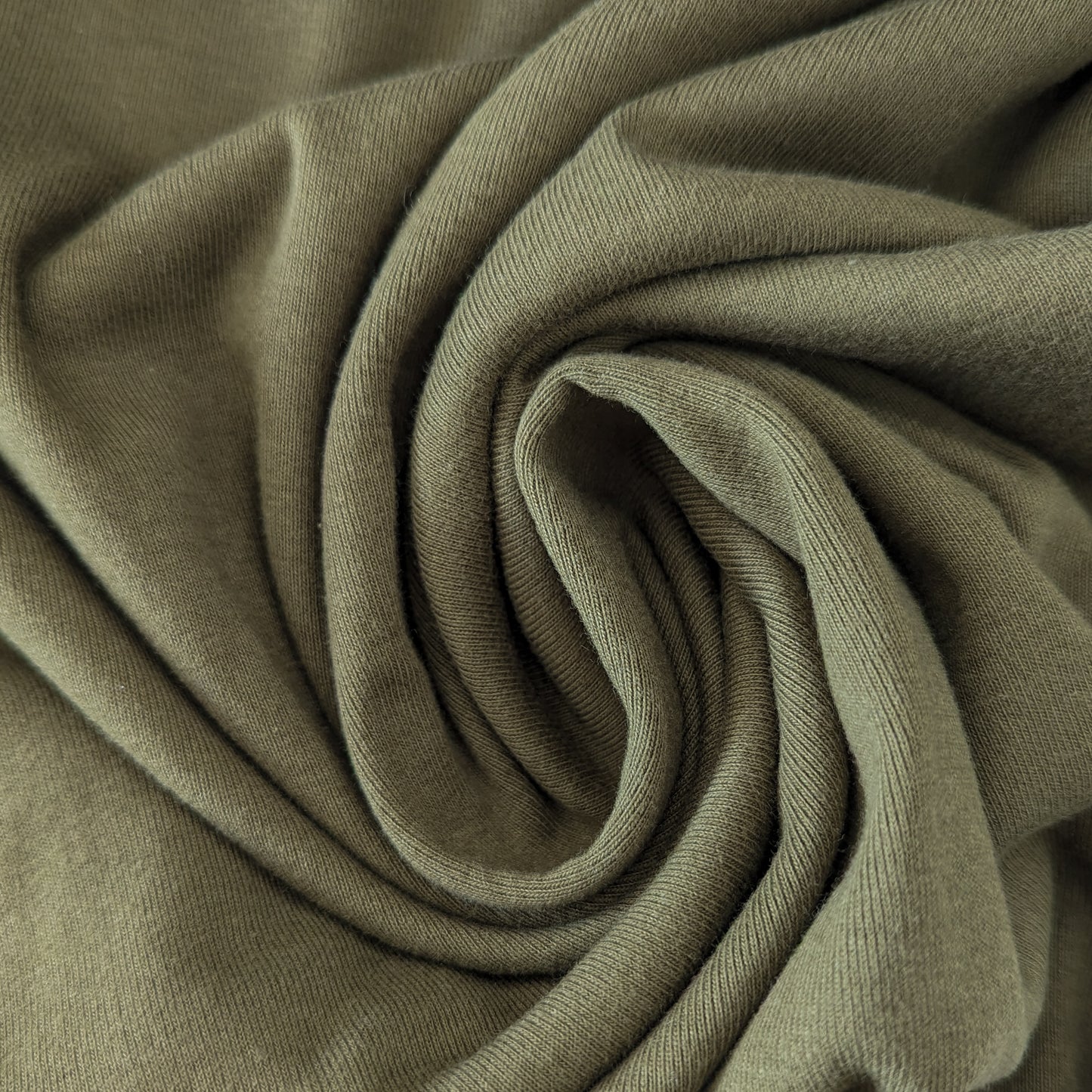 Olive Branch LW Ribstrick fabric, a light green, ribbed knit textile, folded in a spiral.