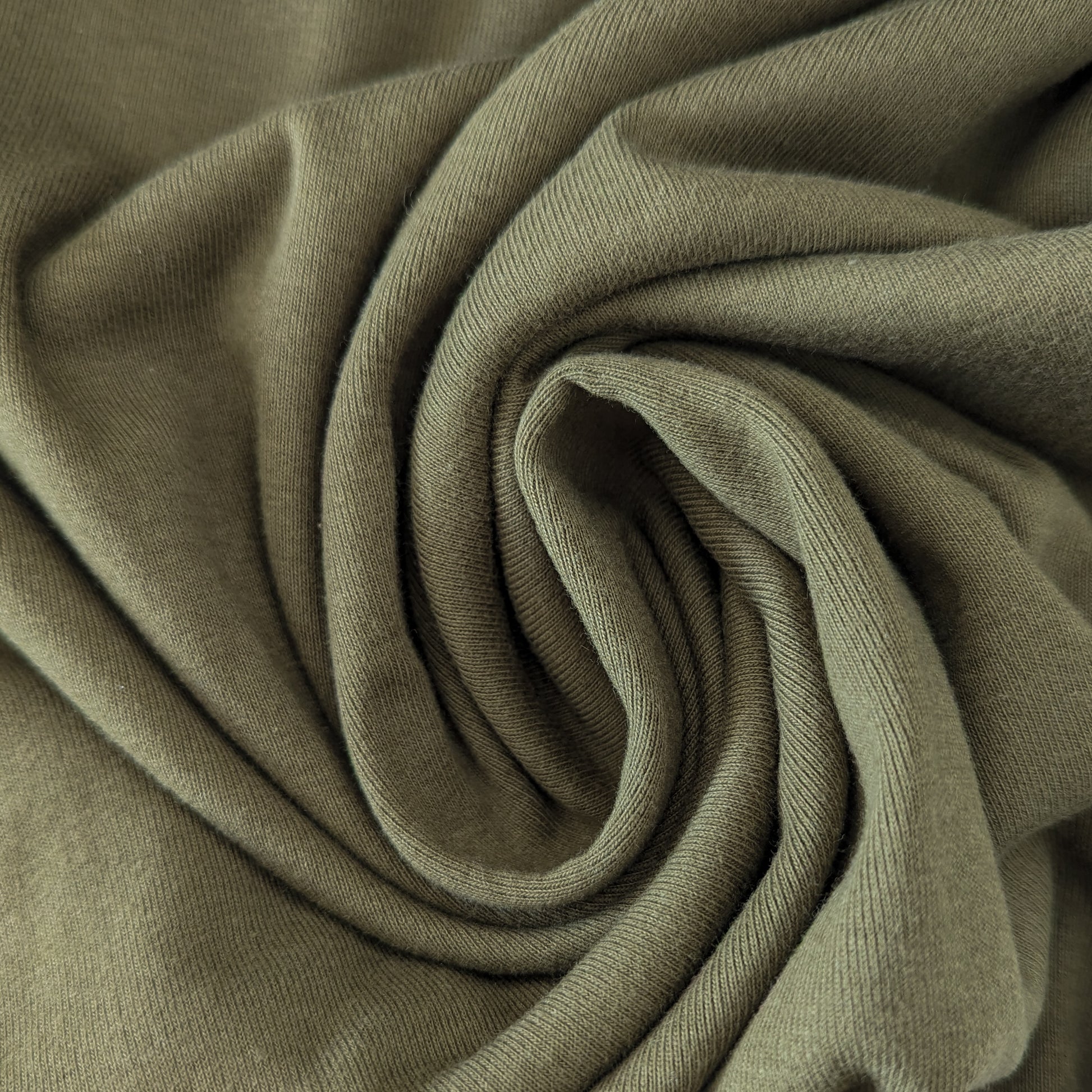 Olive Branch LW Ribstrick fabric, a light green, ribbed knit textile, folded in a spiral.