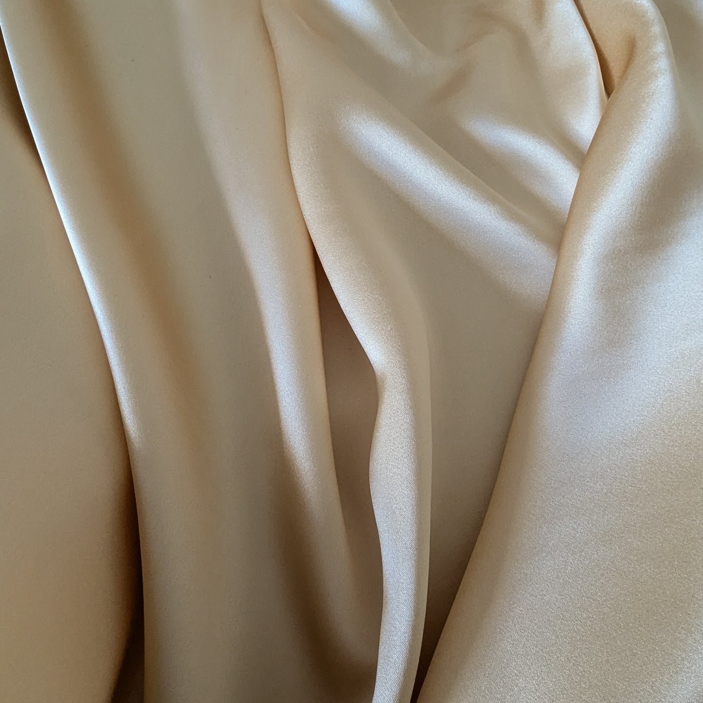 Draped champagne satin silk fabric with a subtle sheen, ideal for elegant garments.