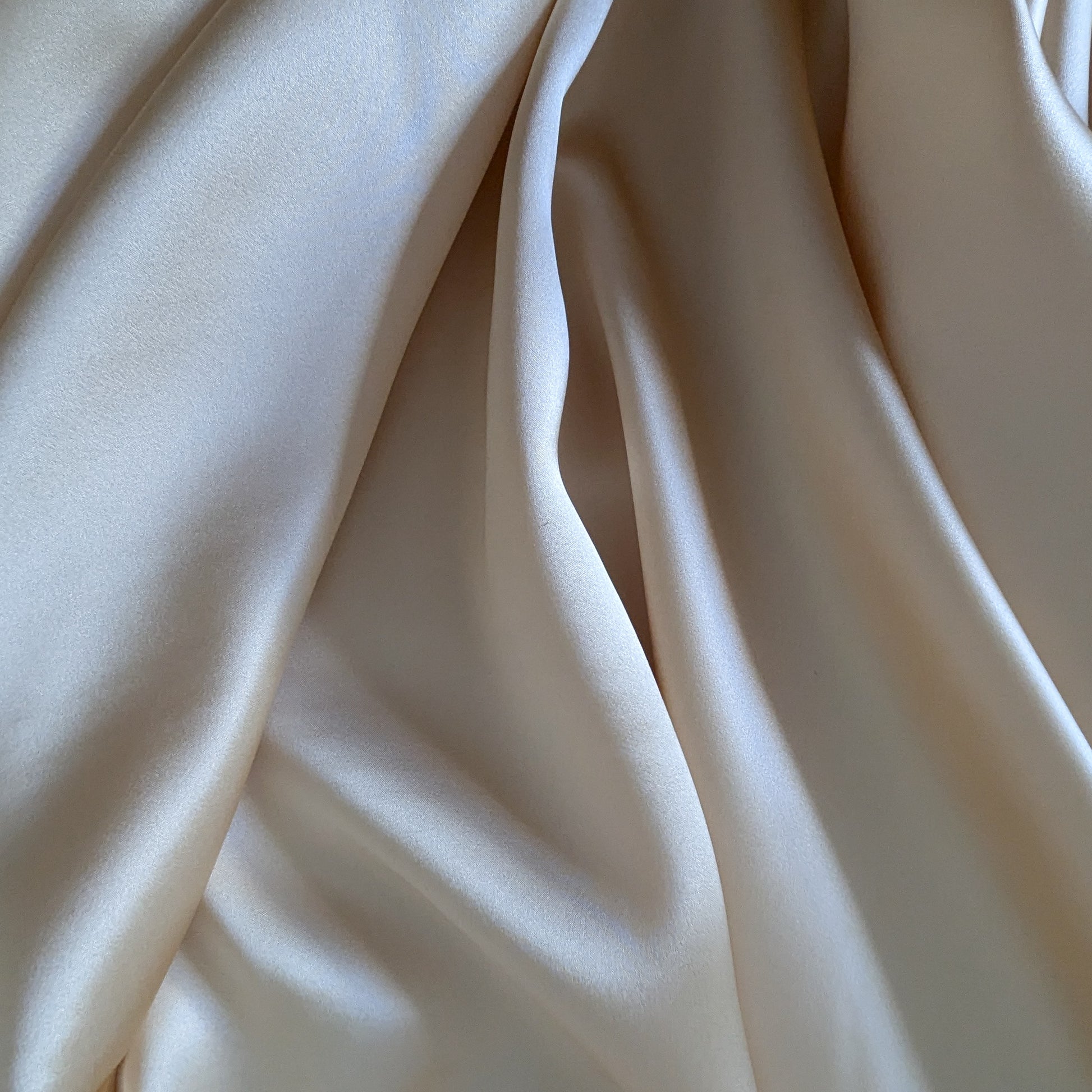 Draped heavy satin silk fabric in a light beige or champagne color, showing its smooth, lustrous texture.