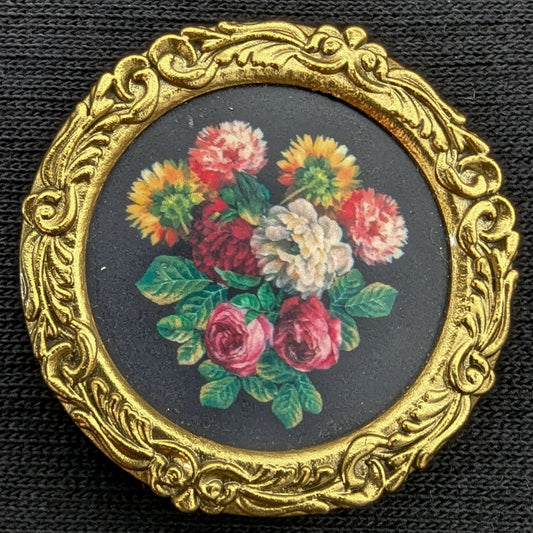 Round gold ornate frame with a miniature floral painting on a black background.