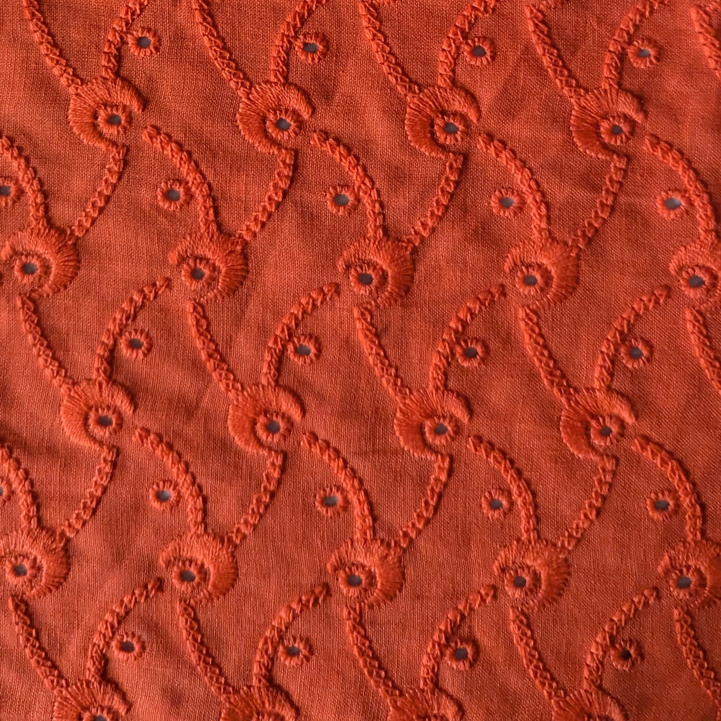 Flame orange Sangallo lace deadstock fabric, 130cm wide, with embroidered eyelets and a repeating curved pattern.