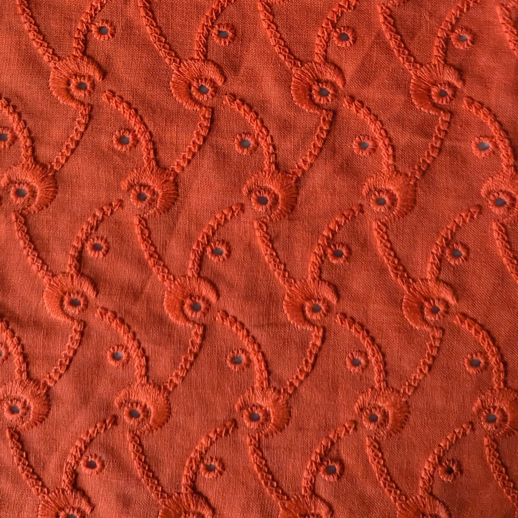 Flame orange Sangallo lace deadstock fabric, 130cm wide, with embroidered eyelets and a repeating curved pattern.