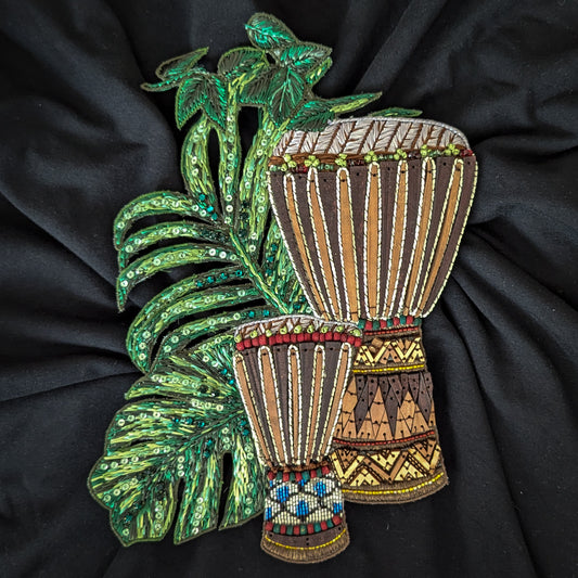 Embroidered patch with two brown drums, green sequined leaves, and colorful bead details on black fabric.