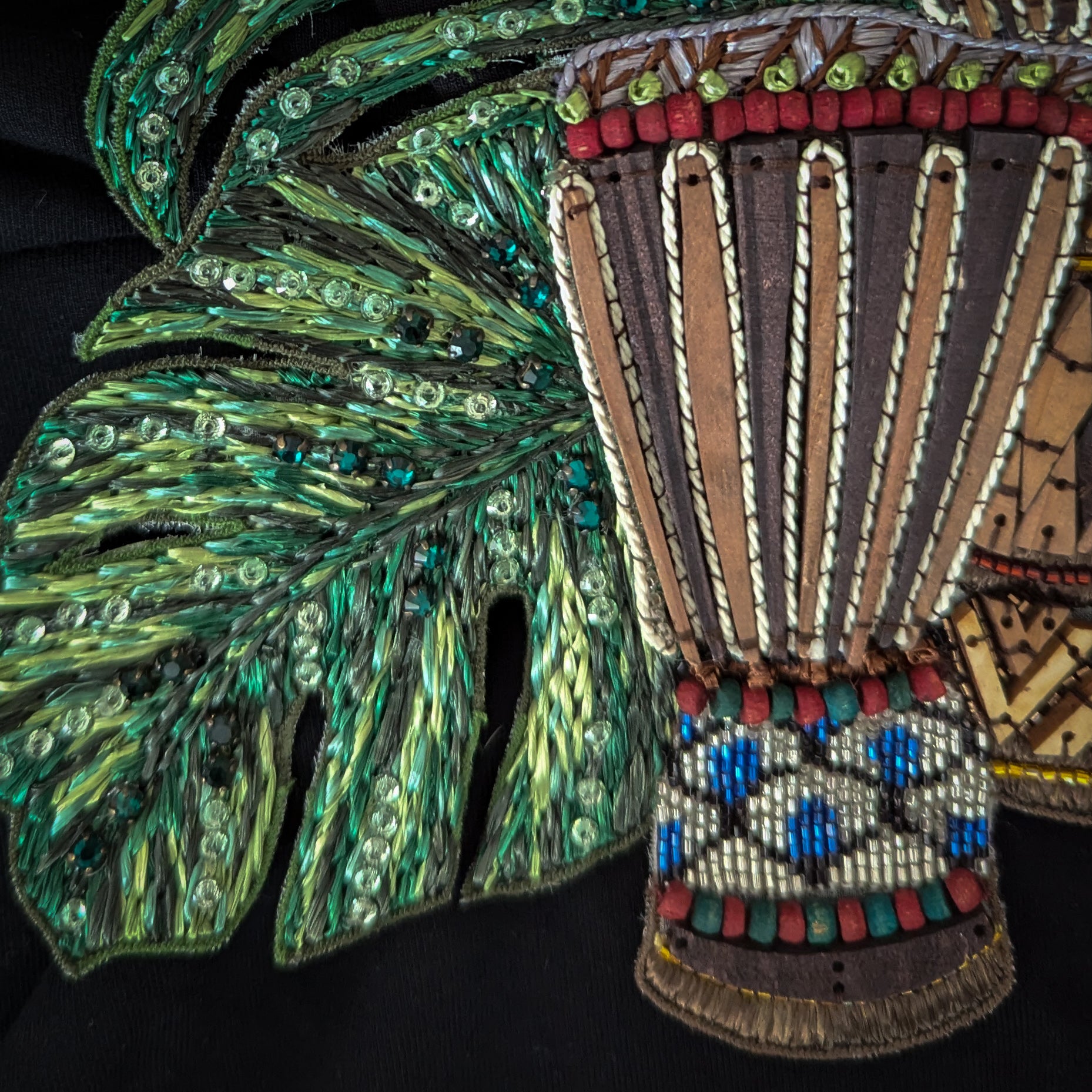 Embroidered patch with a brown drum, green beaded monstera leaf, and colorful accents on black fabric.