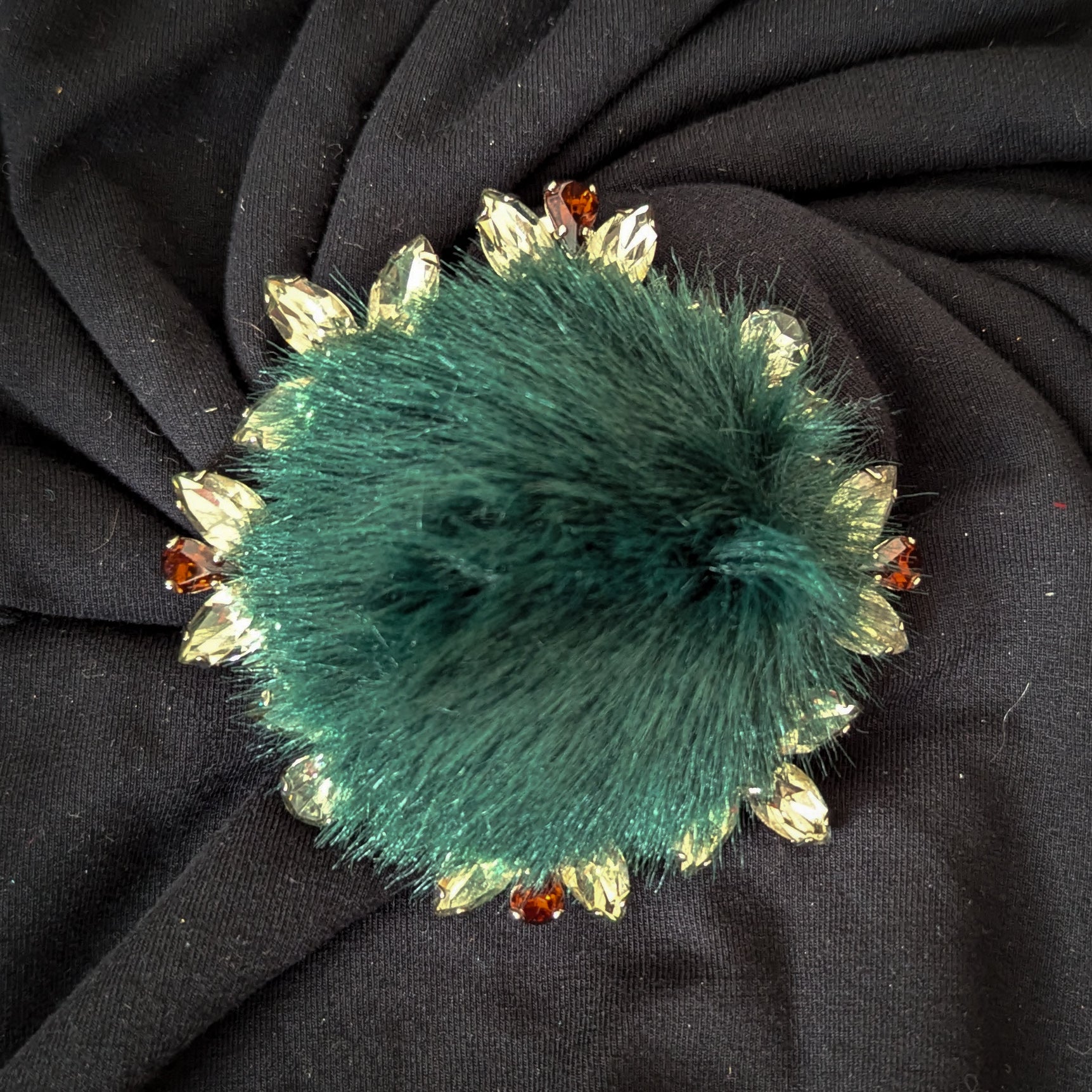Green faux fur ornament with Swarovski-style stones on black fabric.