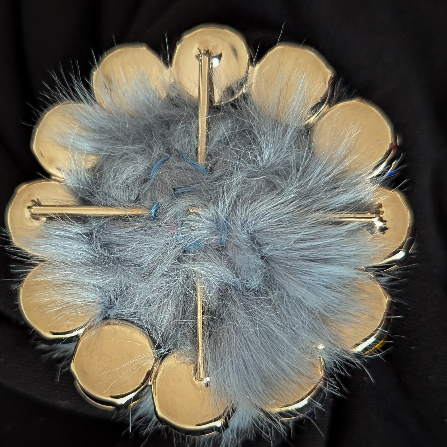 Gold-backed round ornament with light blue fur center and pin attachments.