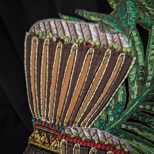 Embroidered drum patch with wood, beads, and green leaves on black fabric, 16x23cm.
