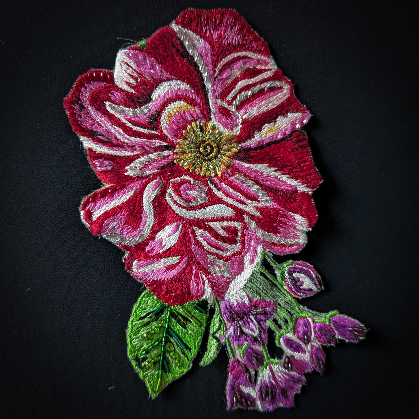 Red and pink embroidered floral patch with white accents, green leaves, and purple beaded details.