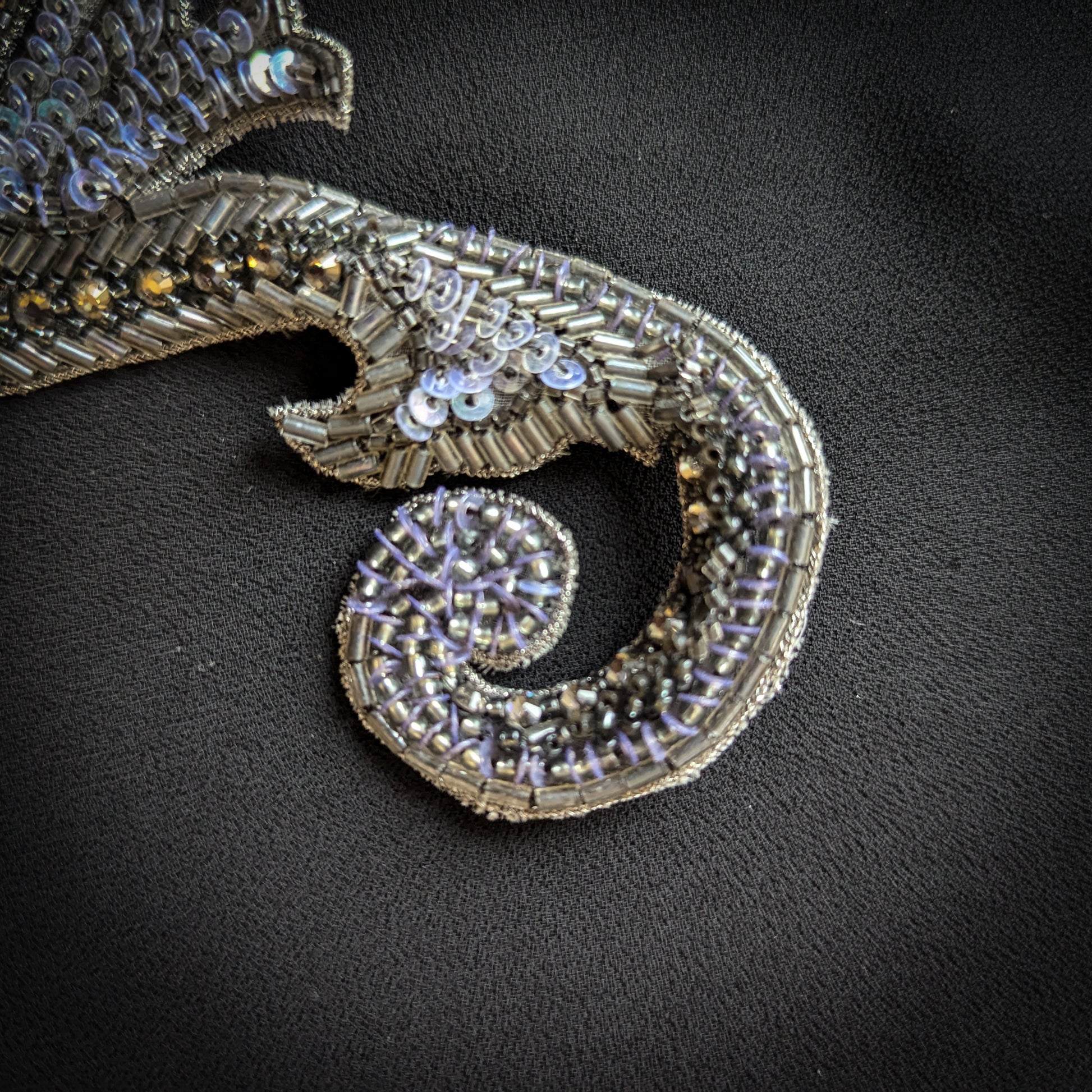 Silver metal and pearl beaded appliqué, 7x17cm, with intricate scroll design on black fabric.