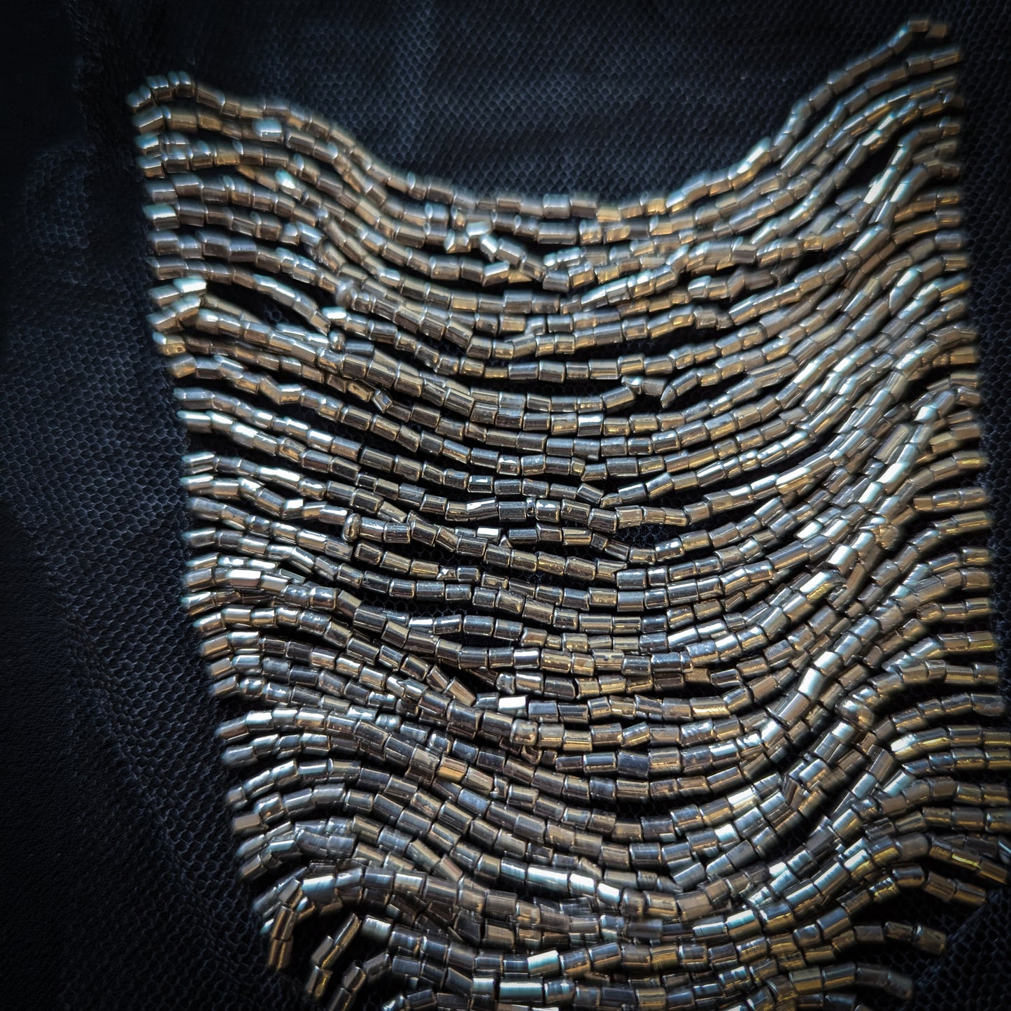 Silver beaded tulle patch in a wavy, textured design on a dark background.