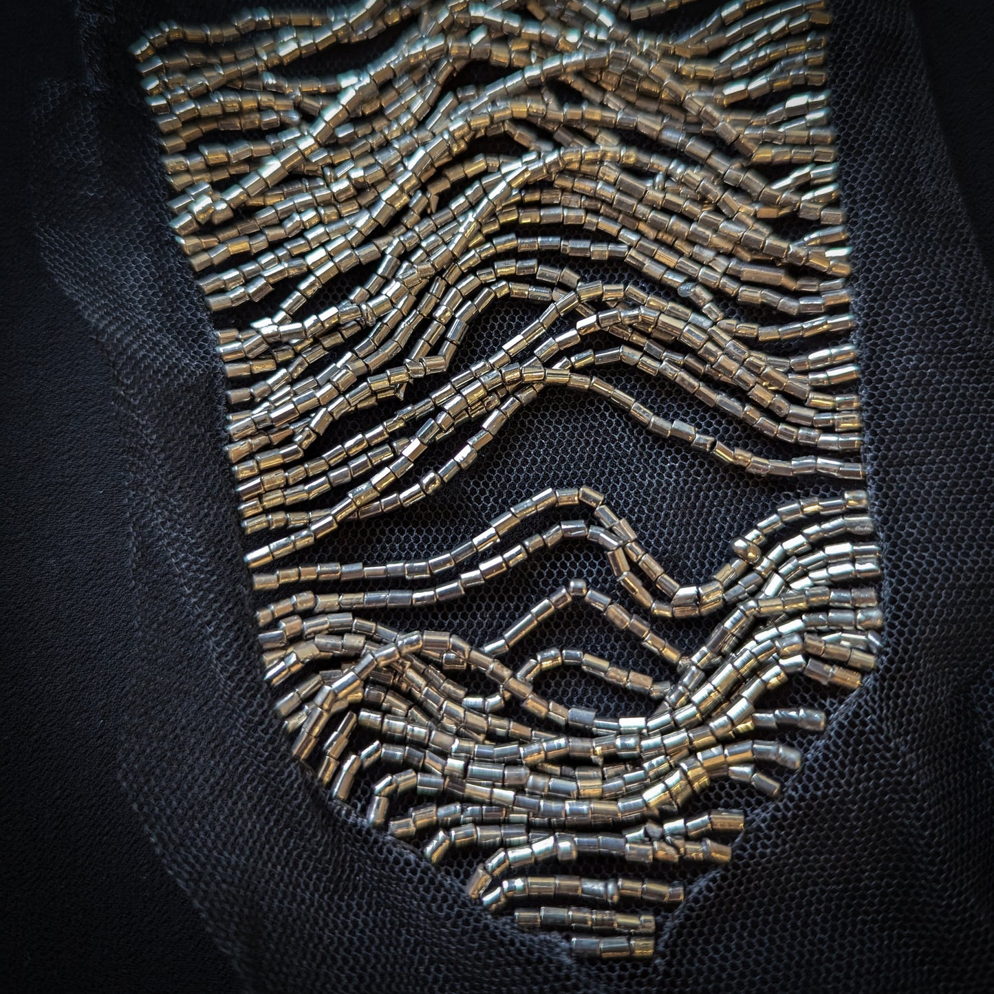 Silver beaded tulle patch in a wavy, abstract design on black mesh.